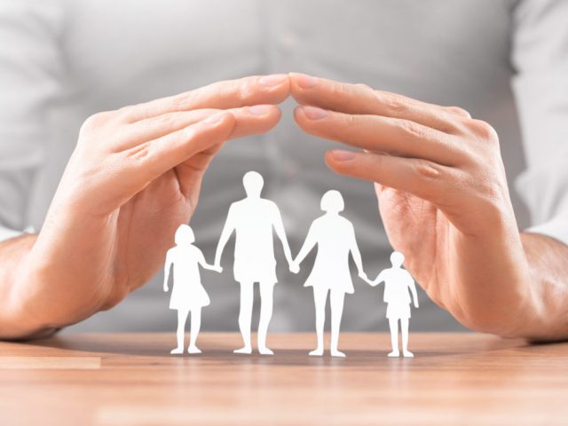 Hands with cut out paper silhouette on table. Family care concept.